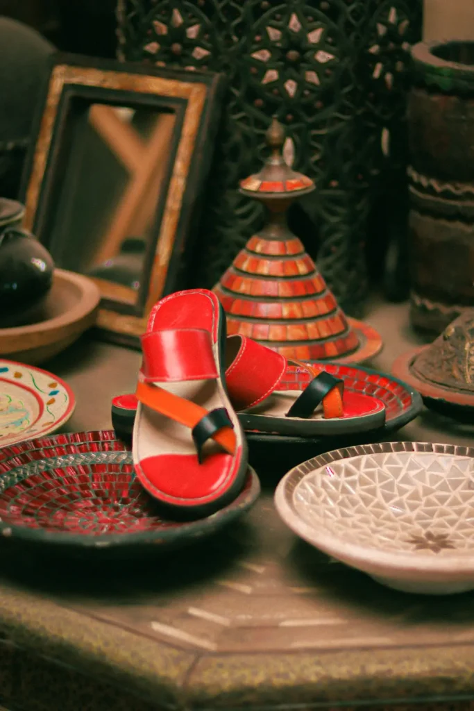 Sandale femme cuire artisanale rouge et orange exposée sur des plats marocains traditionnels à Kasbat Souss, Agadir