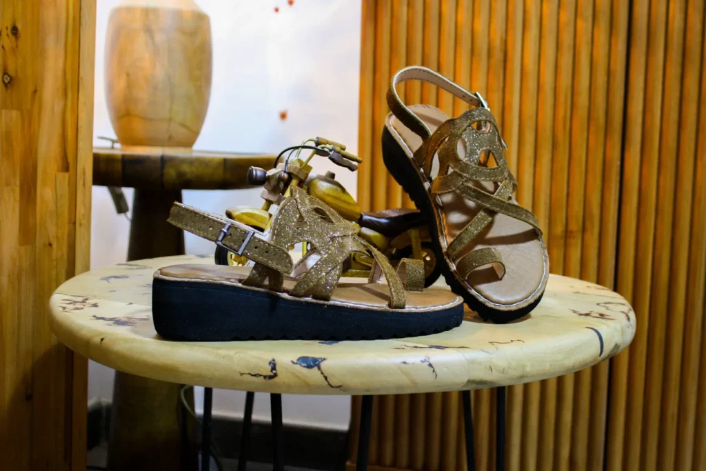 Sandales cuir marron femme artisanales posées sur une table ronde en bois, design élégant avec brides croisées et semelle épaisse – produit fait main par Bagha Shoes