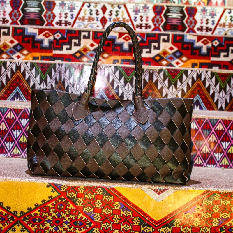 Sac à main en cuir tressé noir et marron sur fond de tapis berbère – artisanat marocain
