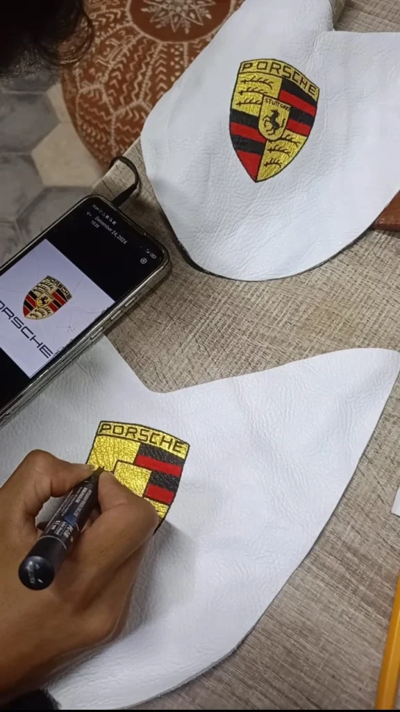 Artisan peignant à la main un logo Porsche sur cuir blanc pour babouche personnalisée homme