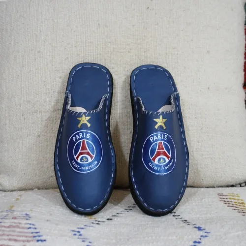 Babouche PSG en cuir bleu posée sur un tapis marocain traditionnel