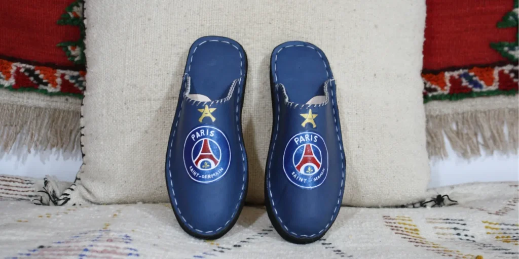 Qu'est-ce que la personnalisation de chaussures babouches en cuir bleu avec logo PSG peint à la main sur fond berbère