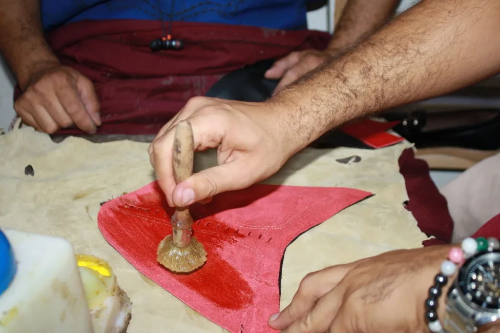 Artisan marocain travaillant le cuir rouge à la main pour fabriquer une babouche homme cuir traditionnelle.